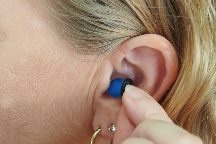 Woman inserting earplug into her ear.