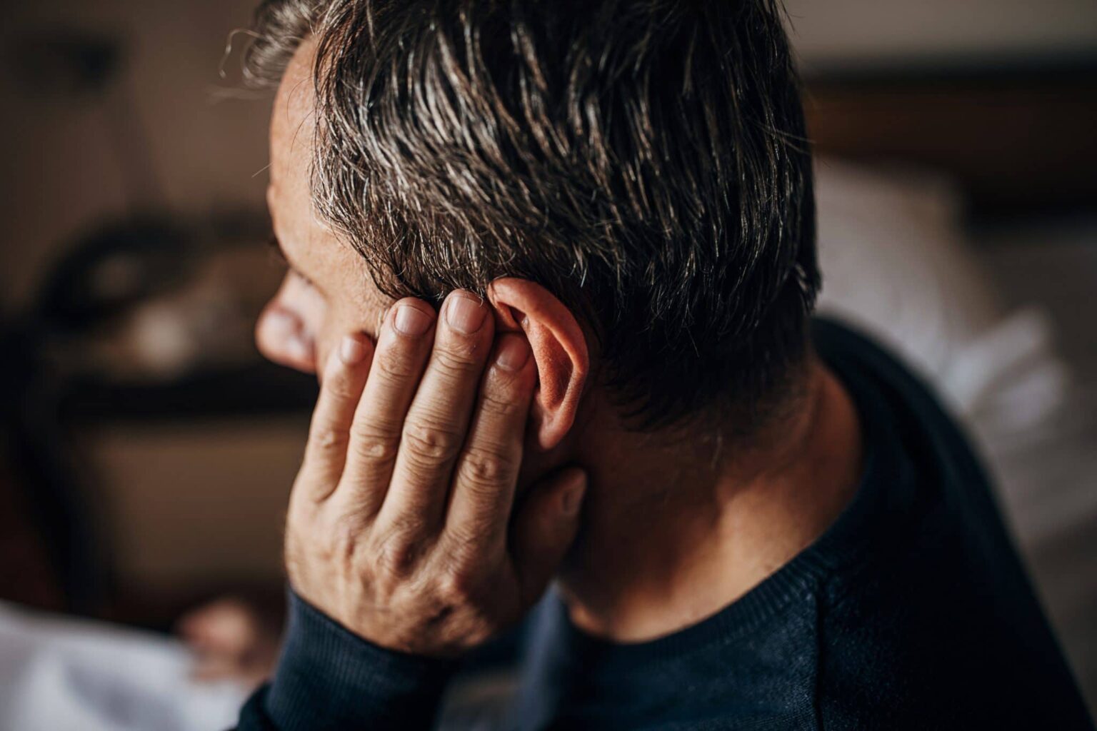 Man rubbing ear from earwax buildup.