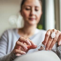 Young Adult Woman inserting battery into the Hearing Aid Young Adult Woman inserting battery into the Hearing Aid