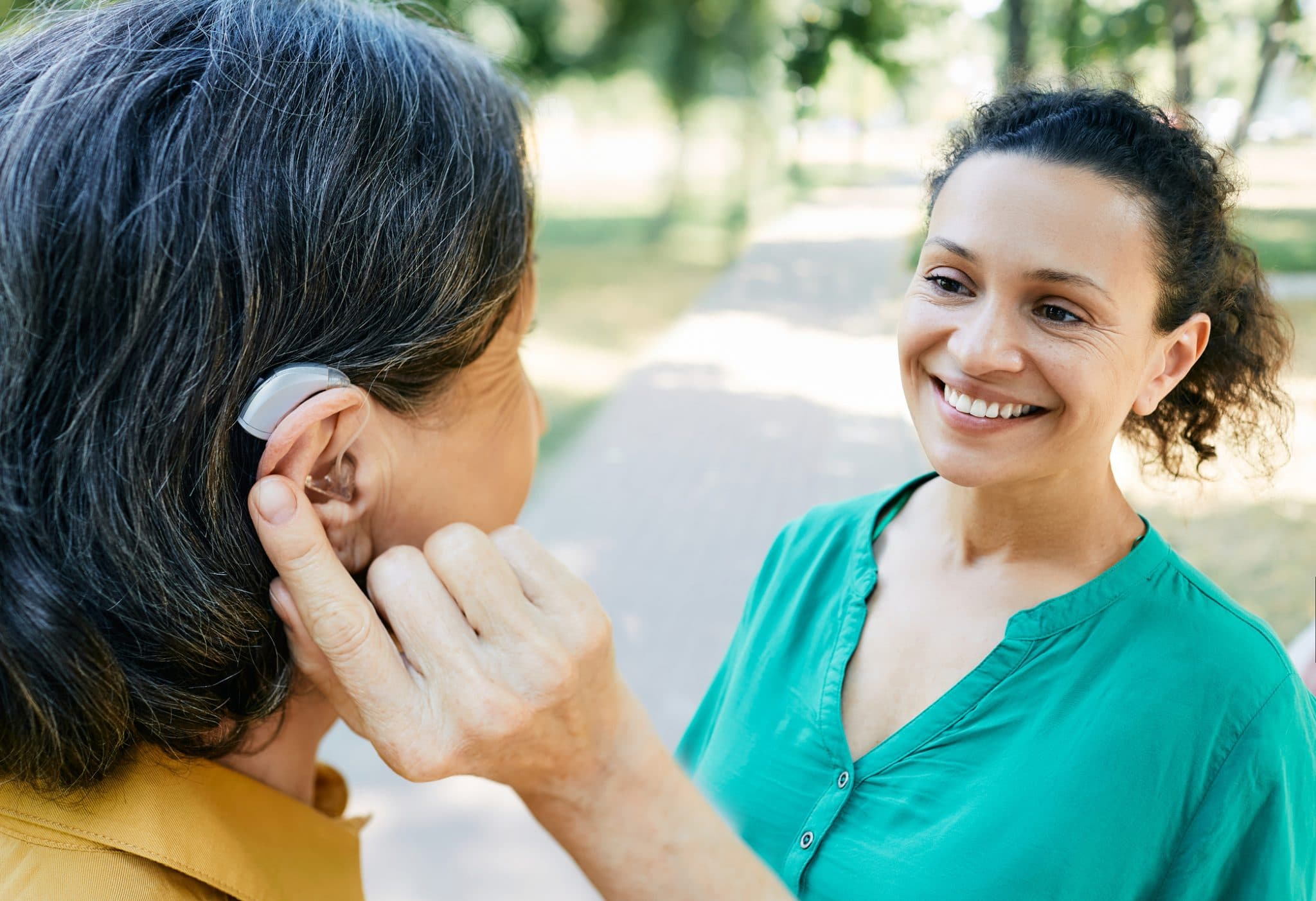 Woman wearing a hearing aid chatting with her friend outdoors.