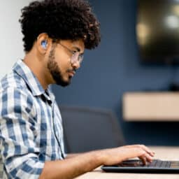Side view of man with a hearing aid working on his laptop.