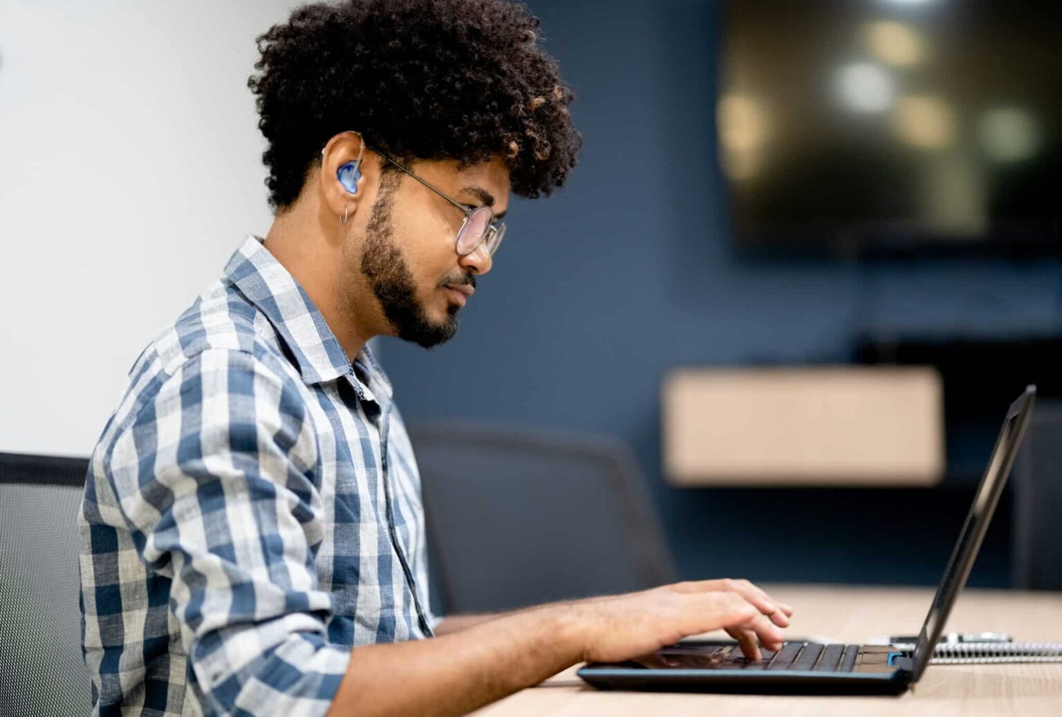 Side view of man with a hearing aid working on his laptop.
