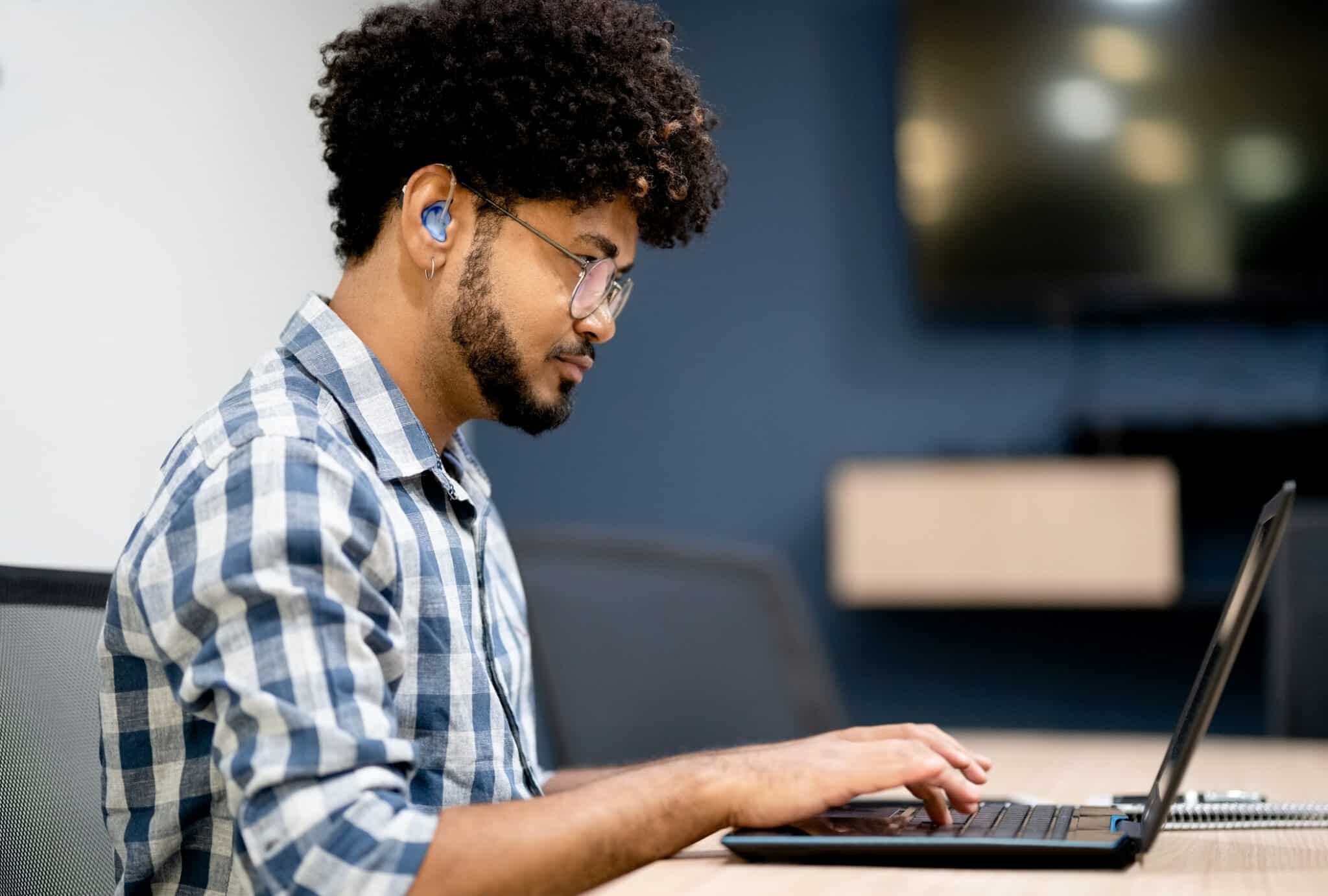 Side view of man with a hearing aid working on his laptop.