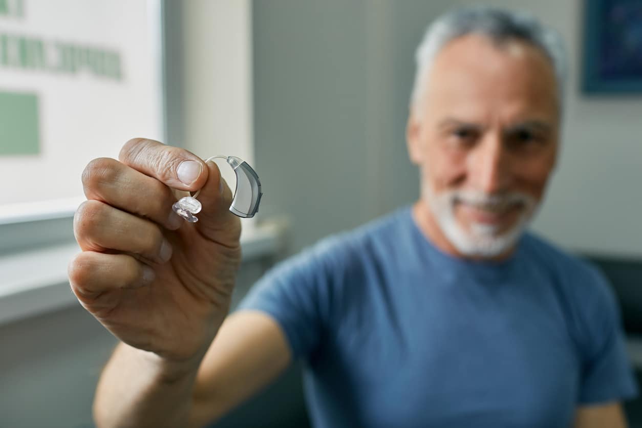 Senior man holding up a BTE hearing aid.