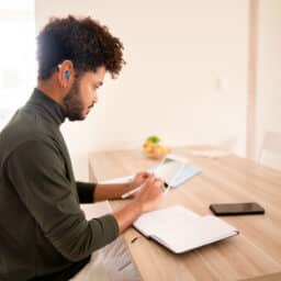 Young man with a hearing aid working on a tablet at home Man connecting hearing aid to his tablet.