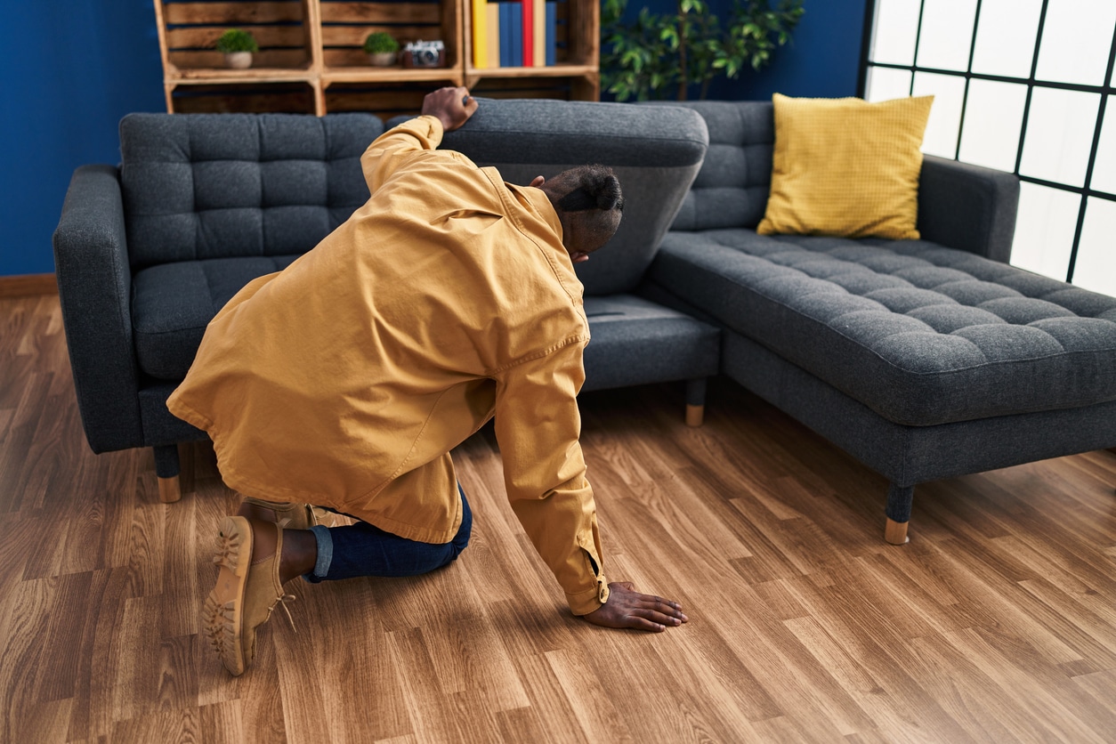 Searching Time Young man looking for something under sofa at home