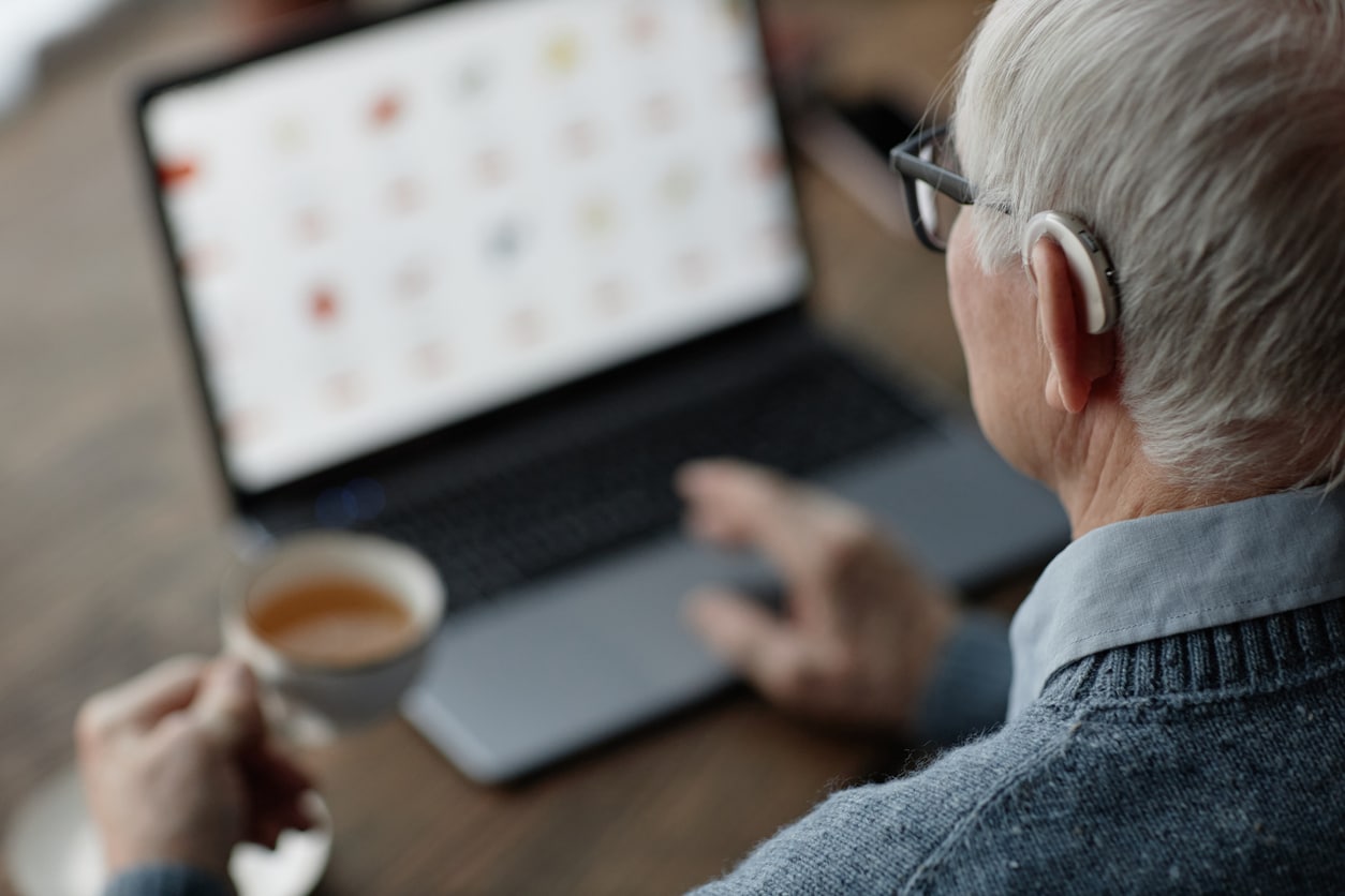 Senior man wearing a hearing aid using his laptop Senior man wearing a hearing aid using his laptop