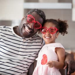 Cute father and daughter in their kitchen wearing Valentines Day heart-shaped sunglasses