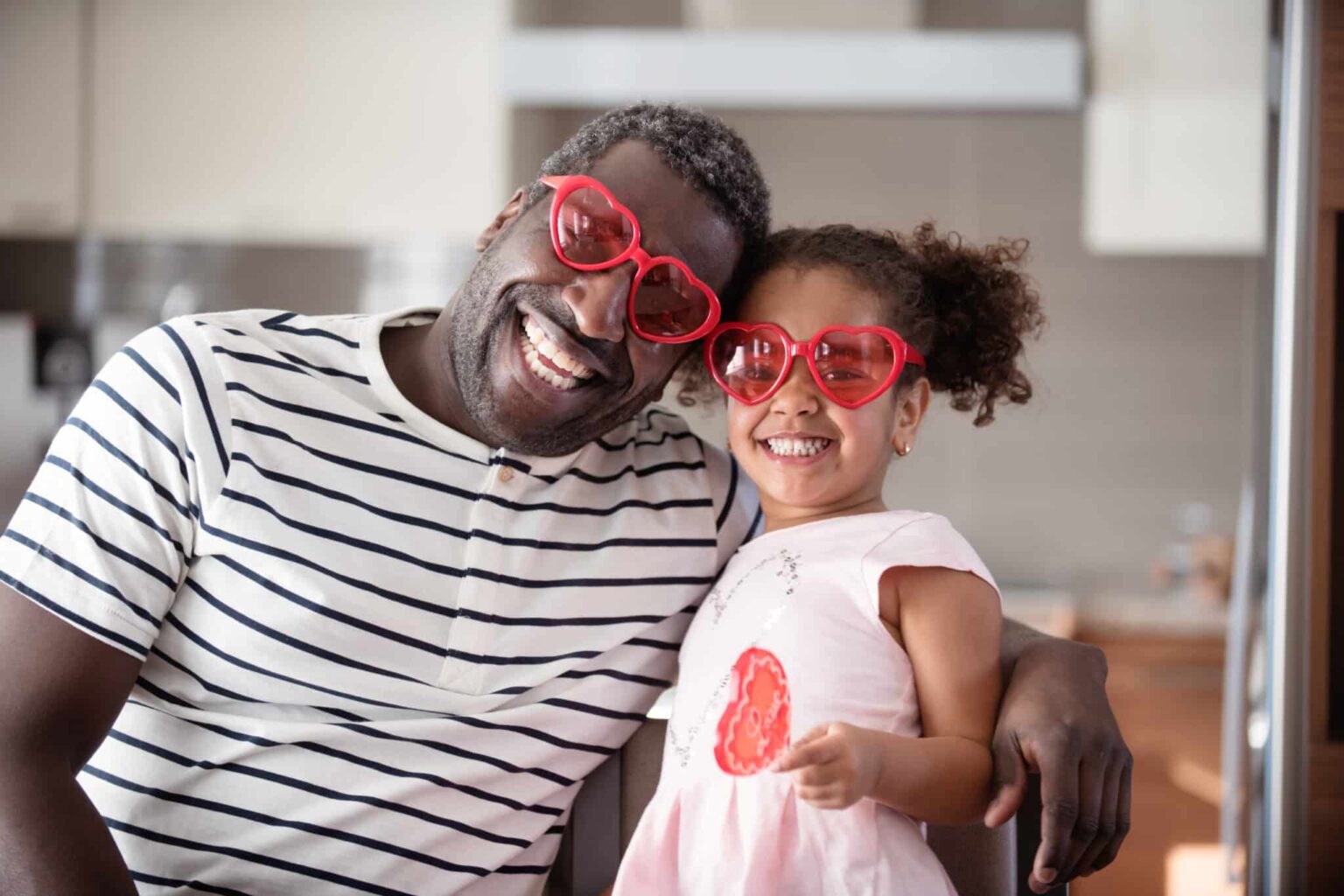 Cute father and daughter in their kitchen wearing Valentines Day heart-shaped sunglasses Cute father and daughter in their kitchen wearing Valentines Day heart-shaped sunglasses