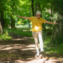 Woman in the woods balancing on a log to show off her good balance.